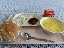 ピンクのトレーに給食が左から時計回りにポテトサラダ、ハンバーグトマトソース、牛乳、コーンポタージュ、丸パンが並んでいる写真