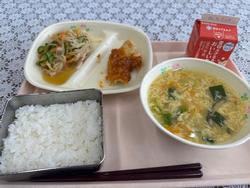 ピンクのトレーに給食が左から時計回りにもやしのナムル、ヤンニョムチキン、牛乳、中華スープ、ごはんが並んでいる写真