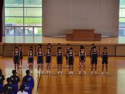 体育館のステージ前で、濃紺のユニフォームを着た複数の生徒たちが整列し、壮行会が行われている写真