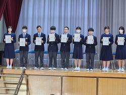 舞台上で任命状を胸の前に持った生徒たちが、横一列に並んで立っている写真