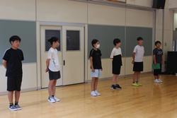 広い室内の入り口前で、6人の小学生たちが等間隔に整列している写真