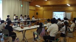 大勢の生徒が参加している、木製の天井と床が特徴的な広い室内で、生徒たちが討論会や発表会を行っている様子の写真