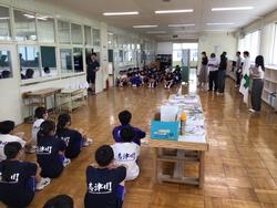 体操服姿の全校生徒が中央に集まる先生方を挟んで向かいあうように整列して座り、話をきいてる避難訓練の様子の写真