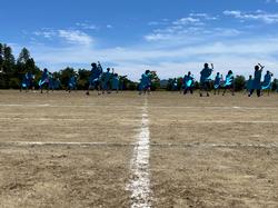 青い服を着た多くの生徒たちがグラウンドに広がり踊りを踊っている写真