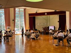 体育館の中で複数のグループが輪になって椅子に座っている様子の写真