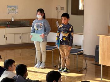 床に座った児童たちの前に立った男女2人の児童が、発表をしている様子の写真