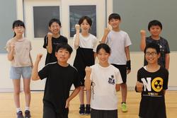 前列に3人、後列に5人の生徒が並び拳を上げて元気いっぱいのポーズでカメラに向かって笑顔を見せている写真