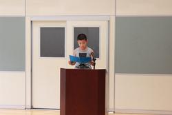 演台のマイクに向かい、青い紙を手に持ちながら真剣な表情で2学期に頑張りたいことを発表している児童代表の男の子の写真