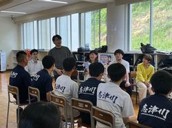 生徒のみなさんが異なる業種の社会人の方々を囲んで座り、自席に立って話をしている男性の話を聞いているドリームクエストの様子の写真