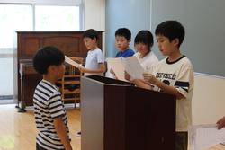 表彰を受ける男子生徒が演台の前に立ち、高学年の男子生徒から表彰を受けている様子を写した写真