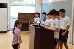 表彰を受ける女子生徒が演台の前に立ち、高学年の男子生徒から表彰を受けている様子を写した写真