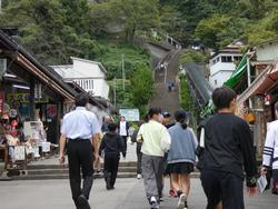 緑の木々の間にある、長い急な階段に向かって、両側に店が並ぶ上り坂の道を歩いている生徒たちの後ろ姿の写真