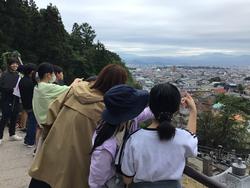 手すりに集まったたくさんの生徒たちが、山頂から見える町の景色を指さしながら眺めている様子の写真