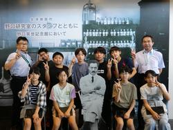 研究室のような白黒写真のパネルの前に、男性の先生2人と9人の生徒たちが並び、前列の生徒は中央に置かれた椅子に腰かけた野口英世の写真パネルを挟んで椅子に座り、全員でピースサインをして写した記念写真