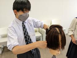 男子生徒がウイッグの髪の毛で練習をしている様子の写真