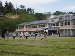複数の生徒たちが、校舎の前のグラウンドを元気いっぱいに走り抜けている様子の写真
