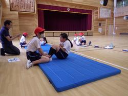 青い体操マットの上で上体を起こしている生徒と、それを支えている生徒が写っている、体力・運動能力テストに取り組んでいる様子の写真