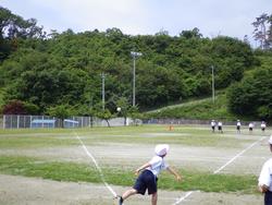 土と芝生のグラウンドで、白い帽子と体操服を着用した子供がボールを投げた瞬間の写真