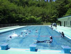 屋外のプールで、水着を着た生徒たちが泳いでいる様子を写した写真