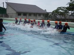 屋外のプールサイドに座った複数の子供たちが、足で水面を激しく蹴って水しぶきをあげている写真