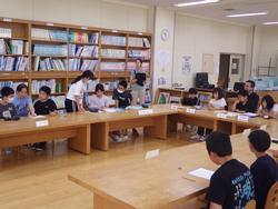 たくさんの本が並んだ部屋で、机に座った複数の小学生が、話し合いをしたりしている様子の写真