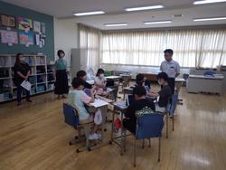 授業中に複数の生徒がグループに分かれて机を囲み、先生が見守る中で課題に取り組んでいる様子を撮影した写真