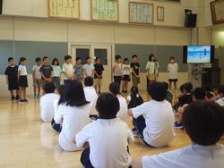 4年生の生徒たちが前方に並んで立ち、座っている生徒の皆さんの前で発表をしている様子を写した写真