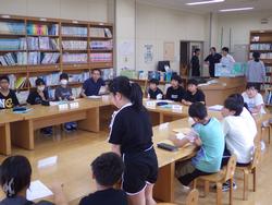 図書室にコの字に設置された机に代表委員の生徒たちが席について話し合いが行われており、手前に立つ女子生徒が発表している様子の写真