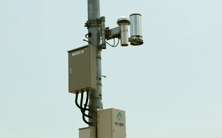 電柱に取り付けられた灰色の観測装置と配電盤、電線が映し出されている写真(南三陸町気象観測システムのサイトへリンク)