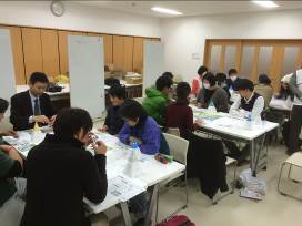 室内に並んだ3つのテーブルに、5人ほどのグループに分かれた参加者たちが座り、ゲームに取り組んでいる様子の写真