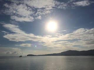 奥に島影が見える穏やかな海に、高く昇った太陽の光が反射している美しい景色の写真
