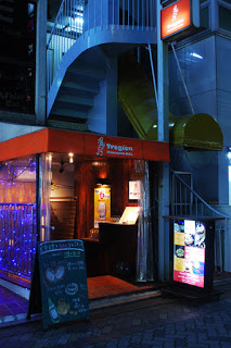 建物の階段下にあるオレンジ色の屋根の飲食店の入り口に、看板やメニューが設置されている写真