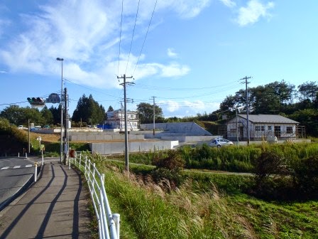歩道のある道路の先に、土を盛って平らにした宅地造成地の区画があり、1件の建設中の家が写された写真
