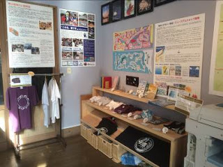 室内の一角に、Tシャツや手ぬぐいなどのグッズが陳列されている、常設ショップの写真