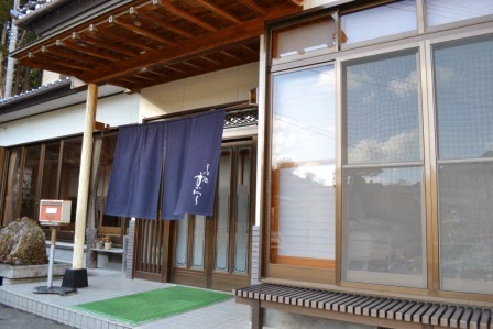 木造の日本家屋の玄関にかかる紺色の暖簾に「すがわら」と書かれており、店の玄関を写した写真