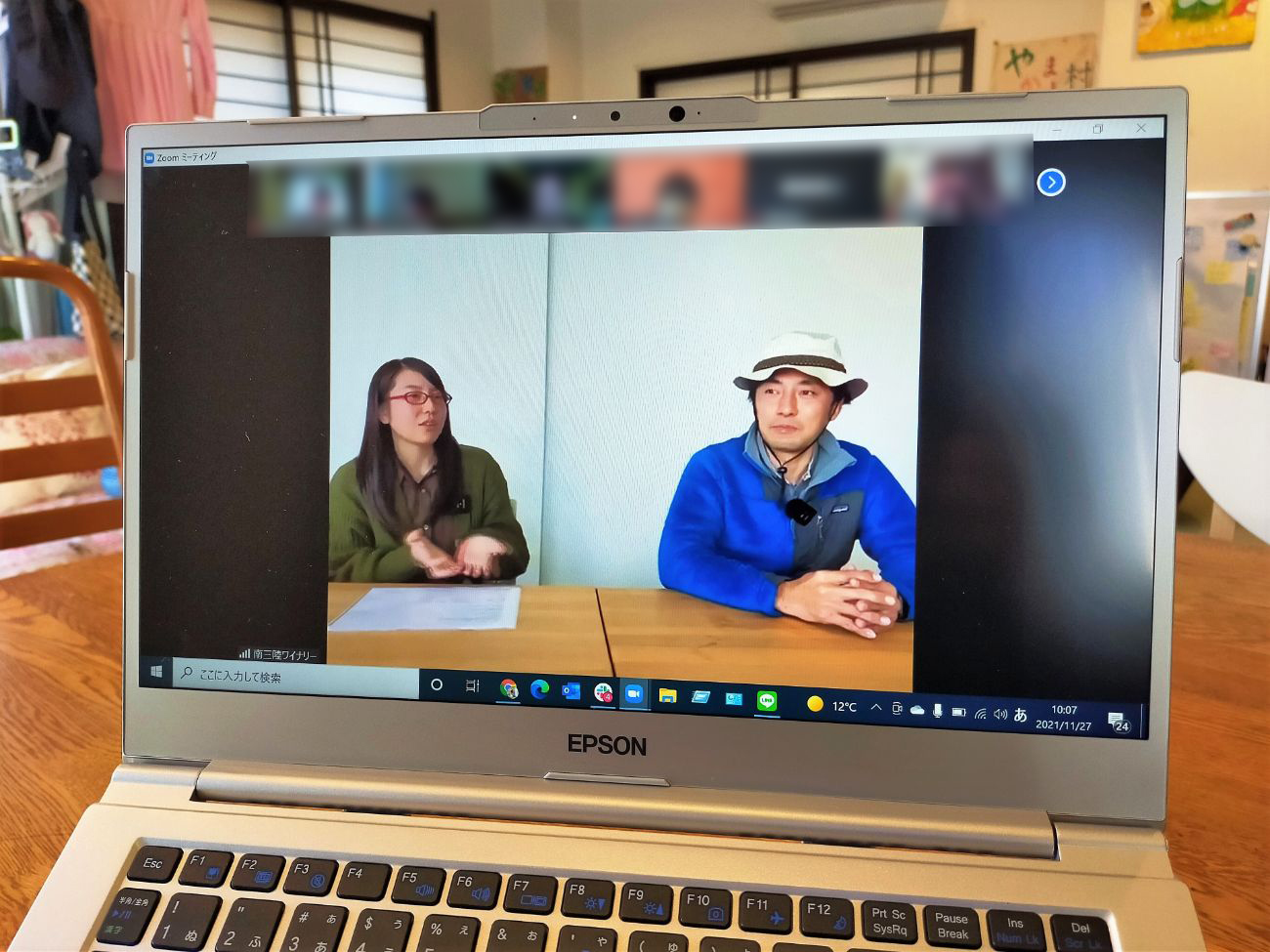 ノートパソコンの画面に、緑のカーディガンを着た及川希さんと青い上着に白い帽子をかぶった佐々木道彦さんが机の前に横に並んで座り、オンライン会議アプリ「Zoom」で話している様子が映し出されている写真