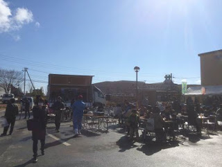 青空の下、たくさんのテーブルと椅子が置かれたスペースが来場者で賑わっている様子の写真