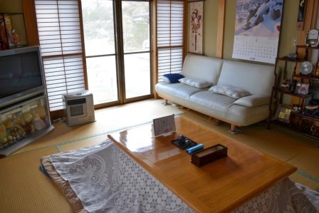 こたつのある畳の部屋に白いソファやテレビが置かれ、家庭的であたたかい雰囲気の客間が広がっている写真