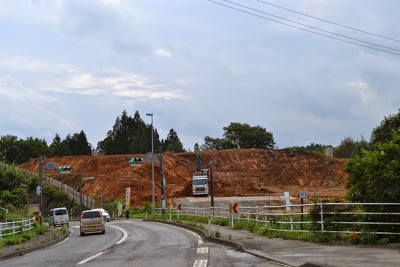 周囲に木々が見え、舗装された道路の先に土が盛られた高台が広がり、重機が稼働している造成工事中の様子の写真