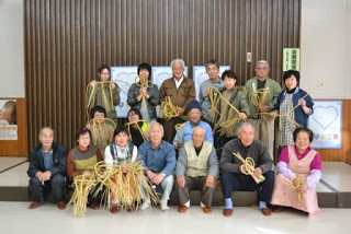 しめ縄作りに参加した方々が完成したしめ縄を手に持ち、笑顔で並んで写っている集合写真