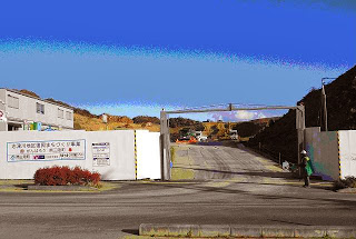 工事現場入口のゲートが開いており、白いフェンスが設置されていて、奥に盛土や作業車両が見える、晴れた日の志津川地区東工区造成工事の開始直後の写真