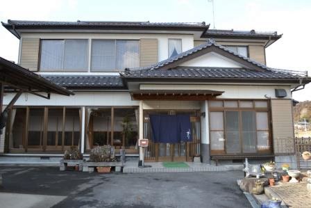 木造の日本家屋の正面に立ち、ガラス戸と青い暖簾がかかった「そば処すがわら」の玄関が見える写真