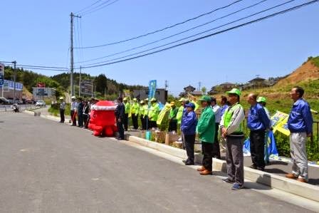 道路脇にオクトパス君、黄緑や青のジャンパーを着た地域住民や警察関係者などが一列に並んで立ち、交通安全街頭キャンペーンを行っている様子の写真