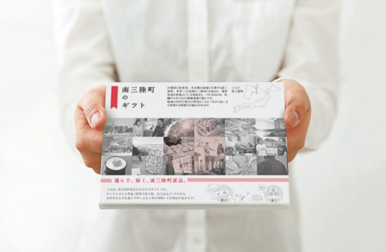 白いシャツを着た人物が両手で持った、南三陸町のギフトと書かれ、18枚の白黒写真がパネル状にのったカタログギフトをアップで撮影した写真