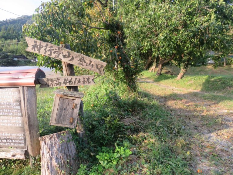 木々に囲まれ、山道の入口に木製の案内板が立っており、「神籠空山登山口」「標高461メートル」と書かれた手書きの木の矢印看板が斜めに取り付けられている写真