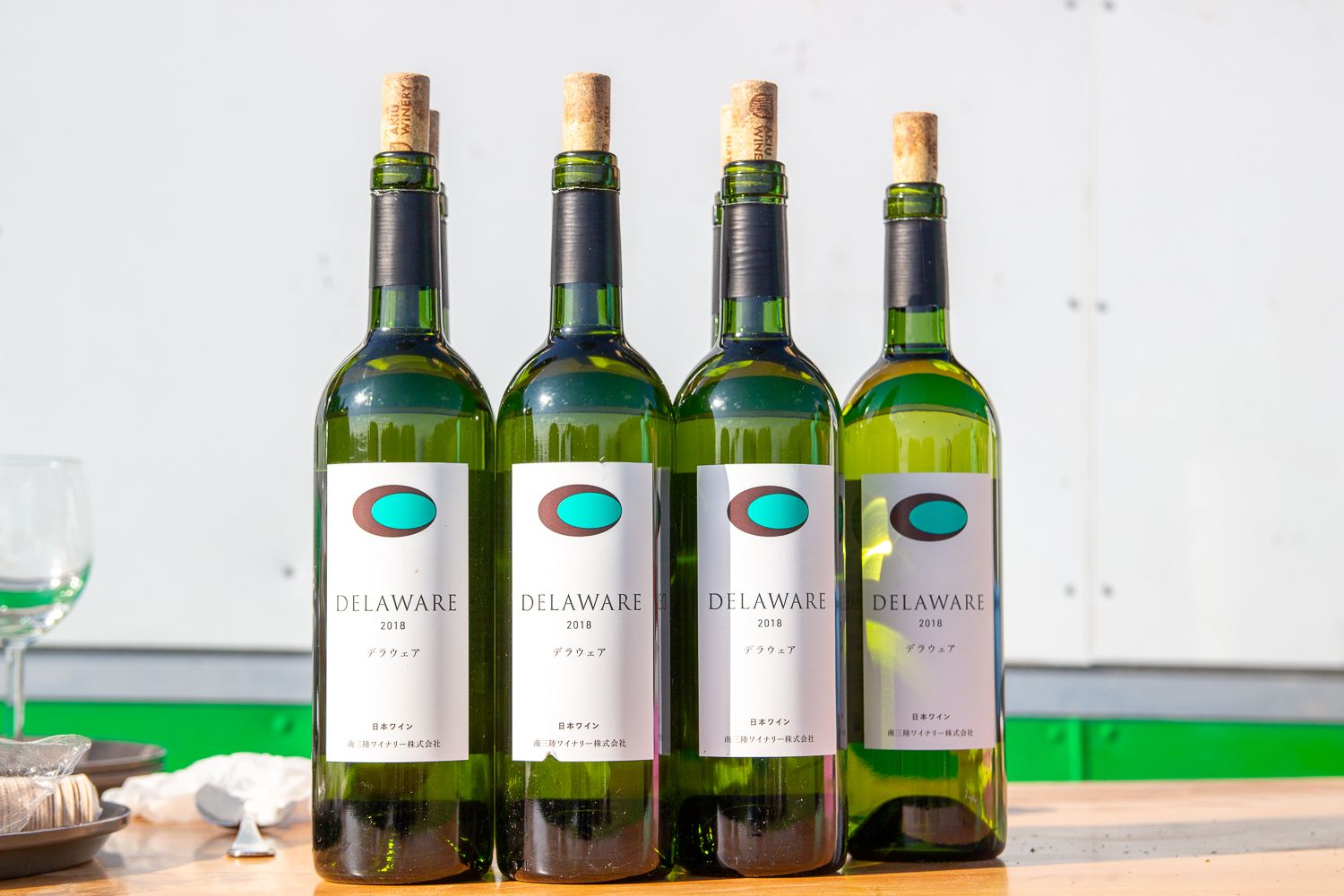 ラベルに「DELAWARE 2018(デラウェア 2018)」と記載されている、4本の緑色のワインボトルがテーブルの上に並んでいる写真