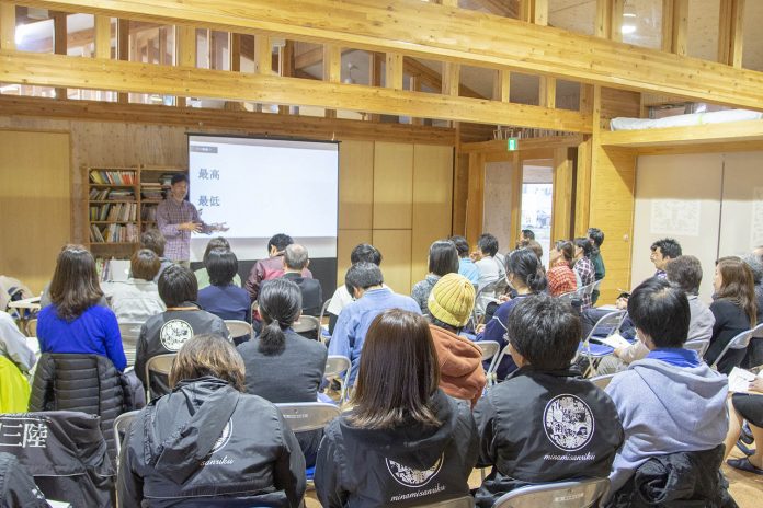 木造の建物内で、多くの人が講師の話を聞いている様子を後方から撮影した写真