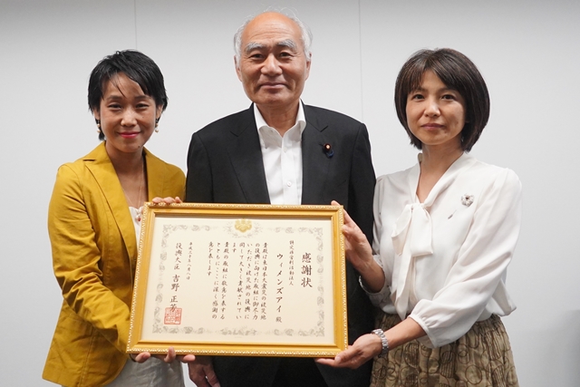 感謝状を額縁に入れて正面に掲げている二人の女性と、笑顔で並ぶスーツ姿の男性の写真