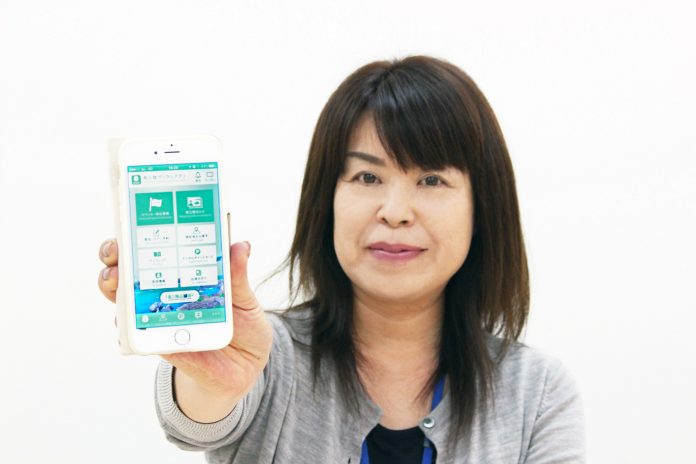 女性が南三陸ポータルアプリを開いたスマートフォンを持ち、画面をカメラに向けている様子をアップで撮影した写真