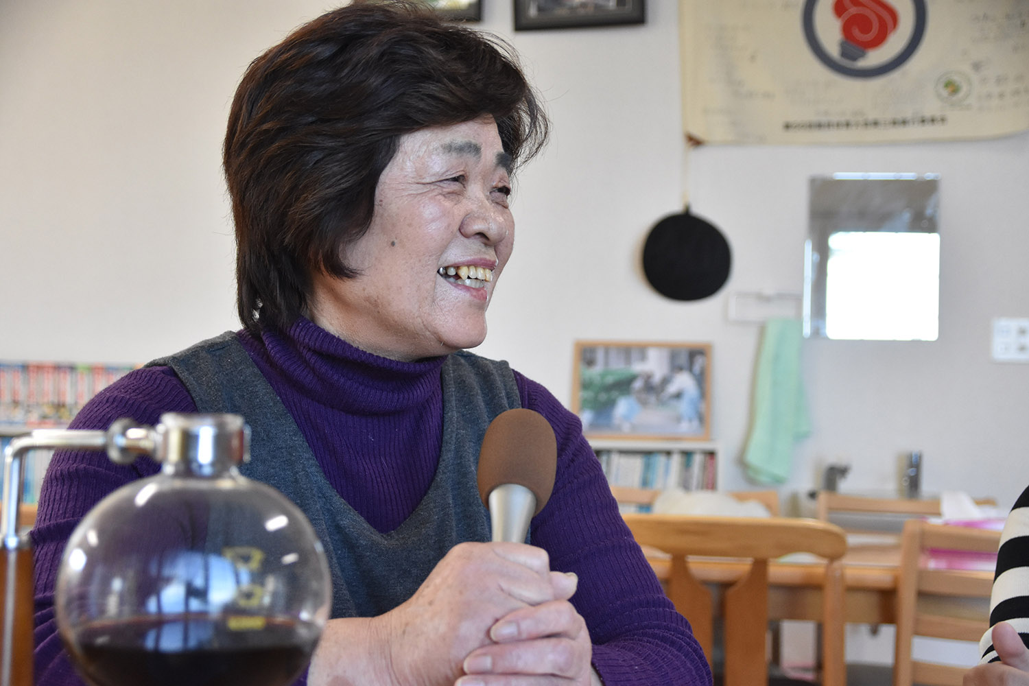 マイクを持ち、コーヒーサイフォンの横で楽しそうに話している西條さんの写真